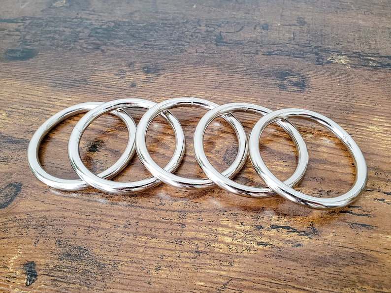 May include: Five silver metal rings of different sizes, stacked on top of each other on a wooden surface.