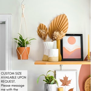 May include: A shelf with a variety of home decor items, including a hanging plant, a vase with dried flowers, a framed print with a sunset landscape, and a framed print with a pressed leaf. The shelf is made of wood and has a light brown finish. The text "CUSTOM SIZE AVAILABLE UPON REQUEST. Please message me with the specific lengths." is visible on the image.