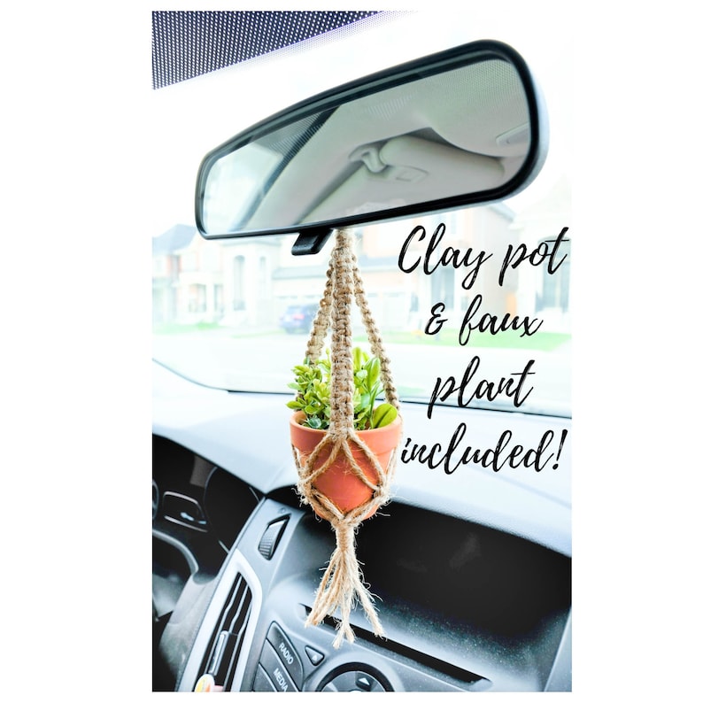May include: A small terracotta pot with a faux plant hanging from a macrame plant hanger in a car. The text "Clay pot & faux plant included!" is written on the image.