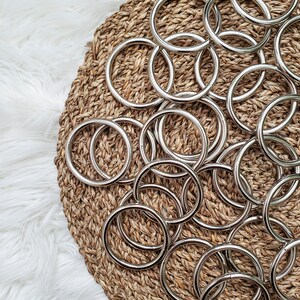 May include: A close-up of a pile of silver metal rings on a woven straw surface. The rings are all the same size and shape, and they are arranged in a random pattern.