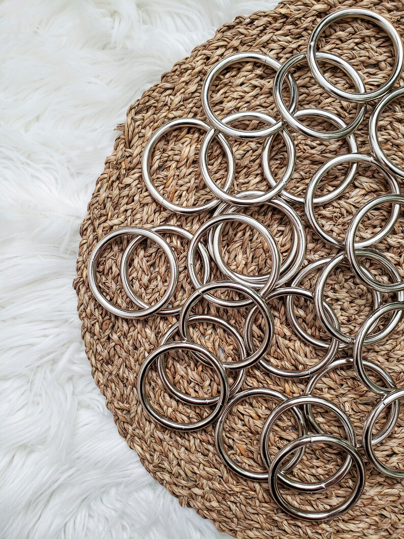 May include: A close-up of a pile of silver metal rings on a woven straw surface. The rings are all the same size and shape, and they are arranged in a random pattern.