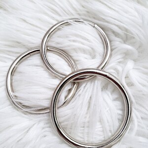 May include: Three silver metal rings, also known as D-rings, are shown on a white fluffy surface. The rings are different sizes and are stacked on top of each other.