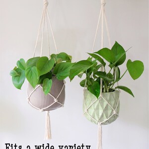 May include: Two macrame plant hangers with white cotton cord and tassels, each holding a potted plant. The plant on the left is in a gray pot, and the plant on the right is in a green pot. The text "Fits a wide variety of pot sizes due to its design!" is at the bottom of the image.