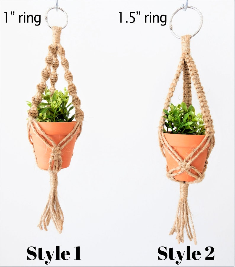 May include: Two macrame plant hangers with different sized rings. The left hanger has a 1 inch ring and the right hanger has a 1.5 inch ring. Both hangers are made with natural jute rope and have a tassel at the bottom. The hangers are holding small terracotta pots with green plants.