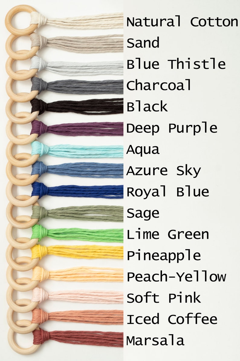 May include: A set of 14 wooden rings with different colored yarn tassels attached. The colors include natural cotton, sand, blue thistle, charcoal, black, deep purple, aqua, azure sky, royal blue, sage, lime green, pineapple, peach-yellow, soft pink, iced coffee, and marsala.