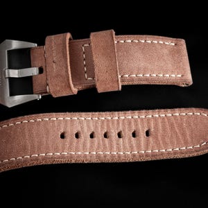 May include: Close-up of a brown leather watch strap with white stitching. The strap has a silver buckle and a textured surface. The brand name "THOMAS ARTISAN STRAPS" is visible.
