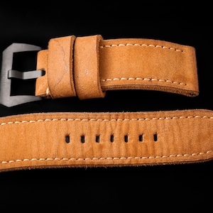 May include: Close-up of a tan leather watch strap with white stitching. The strap has a silver-colored buckle and several holes for adjustment. The strap is made of a soft, textured leather. The brand name "THOMAS ARTISAN STRAPS" is visible in the top left corner.