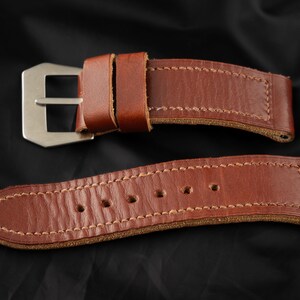 Può includere: Un cinturino da orologio in pelle marrone con una fibbia argentata. Il cinturino ha un bordo cucito ed è progettato per un orologio con una larghezza dell'anse di 20 mm.