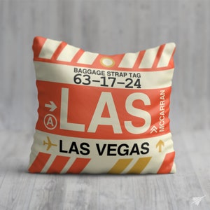May include: A white cushion with a red and yellow luggage tag design. The tag says "BAGGAGE STRAP TAG 63-17-24 LAS LAS VEGAS MCCARRAN".