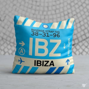 May include: Blue and white luggage tag cushion with the text "IBZ" and "IBIZA" and the code "38-31-96". The tag also has an arrow pointing to the right and the letter "A" in a circle, and an arrow pointing up with the text "FIRST CLASS".