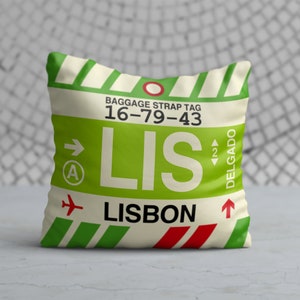 May include: A white cushion with a green and red luggage tag design. The tag has the text "LIS" and "LISBON" with the baggage strap tag number "16-79-43".