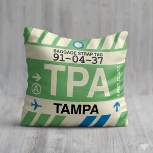May include: A white and green luggage tag with the text "BAGGAGE STRAP TAG 91-04-37 TPA TAMPA" and an arrow pointing to the right. The tag also has a blue circle, a small airplane icon, and the text "FIRST CLASS" written vertically.