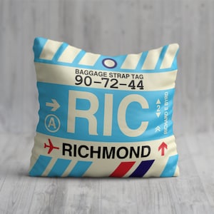 May include: A white and blue throw pillow with a luggage tag design. The tag has the text "RIC" and "RICHMOND" with a baggage strap tag number "90-72-44".