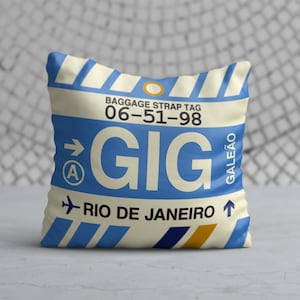 May include: A white and blue throw pillow with a luggage tag design. The tag reads "BAGGAGE STRAP TAG 06-51-98 GIG RIO DE JANEIRO GALEÃO".