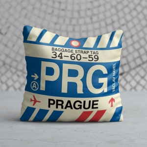 May include: A white and blue throw pillow with a luggage tag design. The tag says "PRG" and "Prague" with the airport code "34-60-59". The tag also says "Vaclav Havel" and has a red airplane icon.