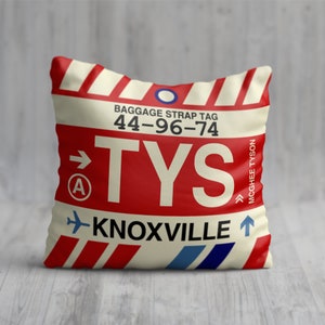 May include: Red, white and blue luggage tag cushion with the text "BAGGAGE STRAP TAG 44-96-74 TYS KNOXVILLE" and an arrow pointing to the right. The tag also has a circle with a letter "A" inside and an arrow pointing upwards.