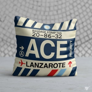 May include: A square pillow with a luggage tag design. The pillow features the text "ACE" in large white letters, with "Lanzarote" below. The design includes a red airplane icon and blue and red stripes. The pillow has a cream background with navy blue accents.