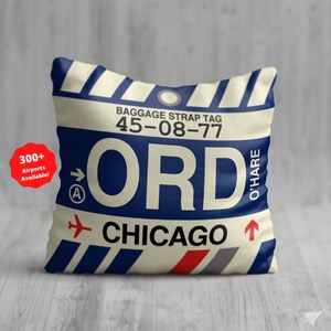 May include: A white and blue throw pillow with a luggage tag design. The tag says "ORD" for O'Hare International Airport in Chicago, Illinois. The tag also has the baggage strap tag number "45-08-77".