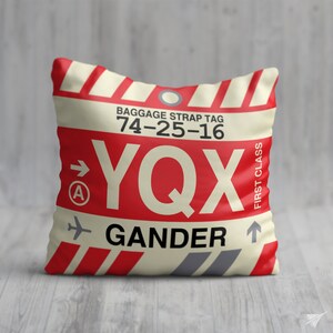 May include: A white and red luggage tag with the text "YQX GANDER" and the baggage strap tag number "74-25-16". The tag also has the text "FIRST CLASS" and an arrow pointing upwards.
