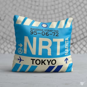 May include: Blue and white pillow with a luggage tag design. The tag says "Baggage Strap Tag 95-06-72 NRT Narita Tokyo".