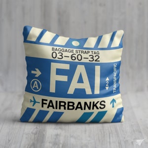 May include: A white and blue luggage tag with the text "BAGGAGE STRAP TAG 03-60-32" and "FAIRBANKS" with the airport code "FAI" in blue. The tag has a blue arrow pointing to the right and a blue arrow pointing up. The tag also has the text "TRANSPACIFIC" in blue.