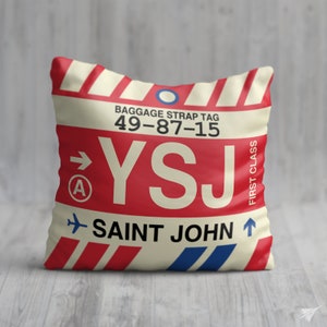 May include: A red, white and blue luggage tag with the text "BAGGAGE STRAP TAG 49-87-15 YSJ SAINT JOHN" and an arrow pointing to the right. The tag also has a circle with a letter "A" inside and the words "FIRST CLASS" written vertically.