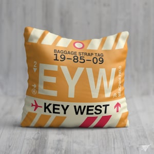 May include: A yellow and white pillow with a luggage tag design. The tag says "Baggage Strap Tag 19-85-09 EYW Key West  Meacham Field".