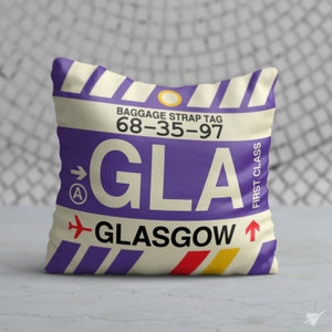 May include: A white and purple pillow with a luggage tag design. The tag says "Baggage Strap Tag 68-35-97 GLA GLASGOW" with an arrow pointing to the right and a small "A" in a circle. The tag also says "First Class" vertically on the right side.