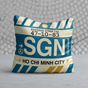 May include: A white pillow with a blue and yellow luggage tag design. The tag says "BAGGAGE STRAP TAG 47-10-83 SGN HO CHI MINH CITY TAN SON NHAT"