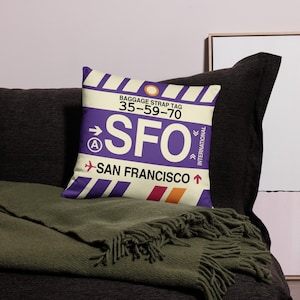 May include: Purple and white throw pillow with a luggage tag design. The tag reads "Baggage Strap Tag 35-59-70 SFO San Francisco International".