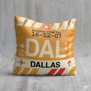 May include: A yellow and white pillow with a luggage tag design. The tag says "BAGGAGE STRAP TAG 16-52-07 DAL DALLAS LOVE FIELD".