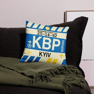May include: A white and blue throw pillow with a luggage tag design. The tag says "BAGGAGE STRAP TAG 25-14-92 KBP KYIV BORYSPIL".