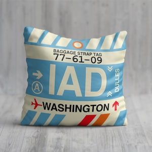 May include: A white cushion with a blue and white luggage tag design. The tag says "Baggage Strap Tag 77-61-09 IAD WASHINGTON DULLES".