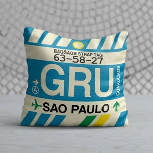 May include: A blue and white luggage tag with the text "GRU" and "SAO PAULO" in black. The tag also has the text "BAGGAGE STRAP TAG 63-58-27" and "GUARULHOS" in white.
