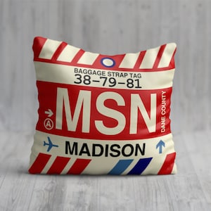 May include: A white and red throw pillow with a luggage tag design. The tag says "Baggage Strap Tag 38-79-81 MSN MADISON DANE COUNTY".