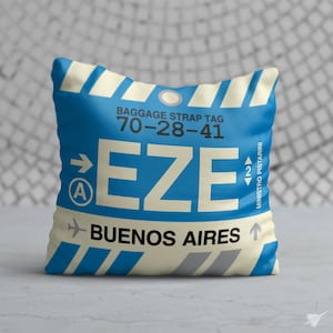 May include: A blue and white luggage tag with the text "BAGGAGE STRAP TAG 70-28-41" and "EZE" in large white letters. Below the letters is the text "BUENOS AIRES" and an arrow pointing upwards. The tag also has a small arrow pointing to the right with the letter "A" inside a circle and a small arrow pointing upwards with the number "2" inside a circle. The text "MINISTRO PISTARINI" is written vertically on the right side of the tag.