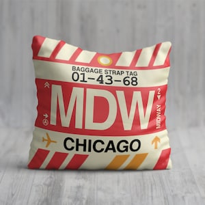 May include: A red and white pillow with a luggage tag design. The tag says "Baggage Strap Tag 01-43-68 MDW CHICAGO" with a small airplane icon and an arrow pointing up.
