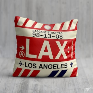 May include: A white and red pillow with a luggage tag design. The tag says "Baggage Strap Tag 98-13-08 LAX Los Angeles International".