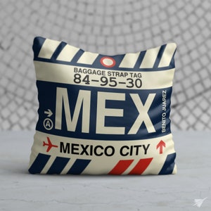 May include: A white cushion with a blue and red luggage tag design. The tag reads "BAGGAGE STRAP TAG 84-95-30 MEX MEXICO CITY" with a red aeroplane icon and an arrow pointing to the right. The tag also says "BENITO JUAREZ" on the right side.