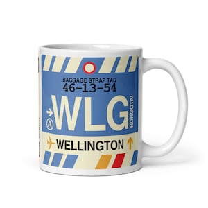 May include: White ceramic mug with a blue and yellow luggage tag design. The tag says "Baggage Strap Tag 46-13-54 WLG Rongotai Wellington".