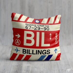 May include: A white pillow with a red and white striped design. The pillow has a luggage tag design with the text "BAGGAGE STRAP TAG 67-29-90 BIL BILLINGS" and a red airplane icon.
