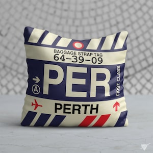 May include: A cream-coloured pillow with a blue and white striped design. The pillow features a luggage tag with the text "BAGGAGE STRAP TAG 64-39-09 PER" and the word "PERTH" below. The tag also has a red arrow pointing up and a small airplane icon.