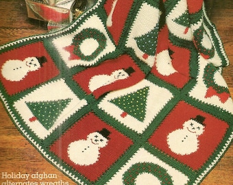May include: A crocheted holiday afghan with a repeating pattern of wreaths, Christmas trees, and snowmen. The afghan is made in shades of red, green, and white.