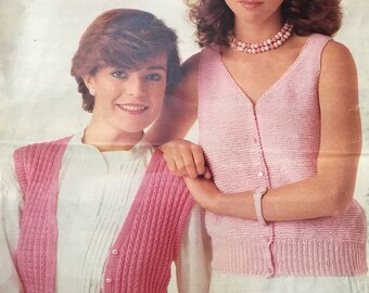 May include: Two women in light pink knitwear. One wears a button-up cardigan over a white blouse, the other a V-neck sleeveless top. Both outfits are paired with white bottoms. The image has a vintage aesthetic.