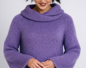 May include: A lilac-colored knit sweater with a wide cowl neck and flared sleeves. The sweater is made of a soft, textured yarn. The model is wearing the sweater. The background is a solid white.