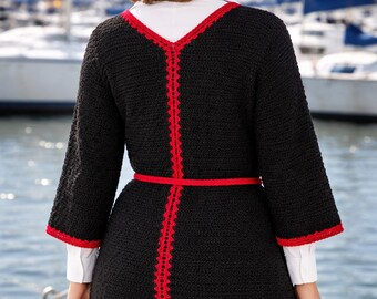 May include: Black cardigan with red trim and a matching belt. The cardigan has three-quarter sleeves and a V-neck. The red trim outlines the edges and seams of the cardigan. The model is wearing a white shirt underneath.