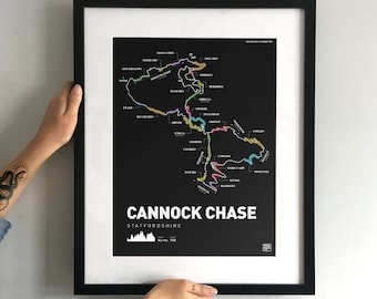 May include: A framed black and white map print of Cannock Chase, Staffordshire. The map features colorful lines indicating trails, with the text "Cannock Chase" in large white letters. The print is held by two hands with tattoos.