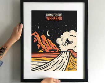 May include: A black framed poster featuring a graphic design of a mountain range, a car driving on a road, and a person riding a bicycle in the air. The poster has the text "Living for the Weekend" in orange and black.