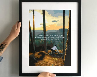 May include: A black framed print with a colorful illustration of a person riding a bicycle through a forest. The print has the text "THERE IS NOTHING QUITE SO WORTHWHILE AS SIMPLY MESSING ABOUT ON BICYCLES".
