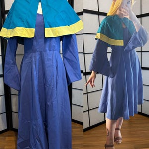 Könnte beinhalten: Ein blaues Kleid mit einem türkisfarbenen und gelben Umhang. Das Kleid hat lange Ärmel und ein tailliertes Oberteil. Der Umhang hat eine Kapuze und einen gelben Saum. Das Kleid wird auf einer Schaufensterpuppe und einer Person gezeigt, die es trägt.